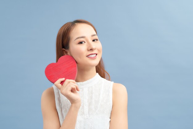 Happy woman hold red heart. Beautiful female model posing on isolated blue background.