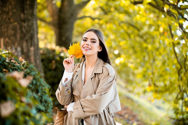 Happy woman holding autumn leafs on face in fall nature portrait of young woman with autumn maple le