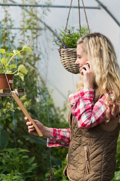 Happy woman holding a clipboard in her green house on the phone