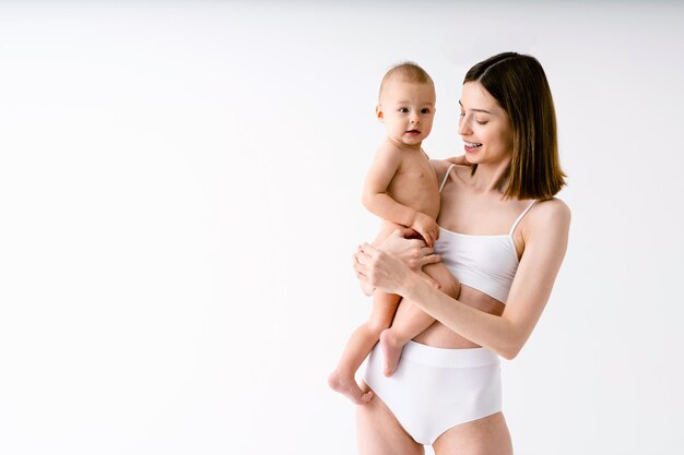 Happy woman holding her baby  on colored background -  Young woman wearing underwear taking care of her little son  - Pregnancy, motherhood, people and expectation concept