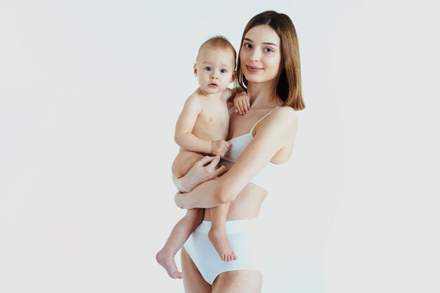 Happy woman holding her baby  on colored background -  Young woman wearing underwear taking care of her little son  - Pregnancy, motherhood, people and expectation concept