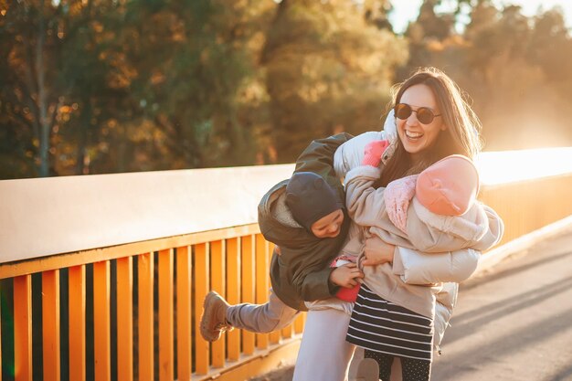 Happy woman holding her kids playing outdoors Family having fun together outside during autumn season