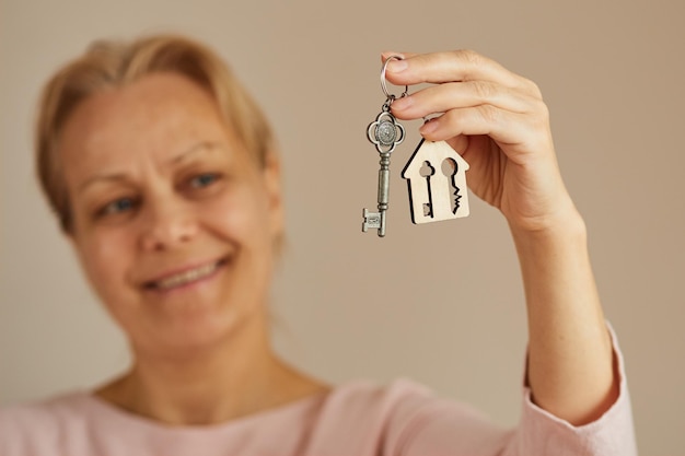 Happy woman holding a house key Key with a keychain in the form of a house Focus on key