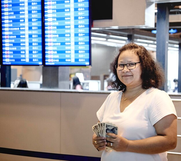 Photo happy woman holding paper currency while standing at airport