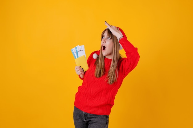 Happy woman holding plane tickets and passport wearing santa hat