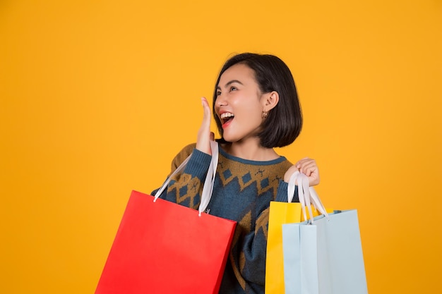 Happy woman holding shopping bags while standing against yellow background