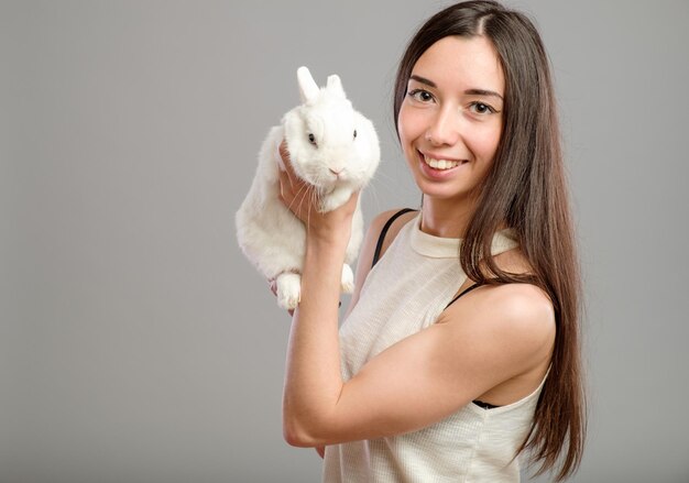 Happy woman holding white rabbit isolated on a gray background