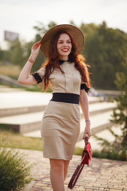 A happy woman, holding a wide hat, poses in a park in summer
