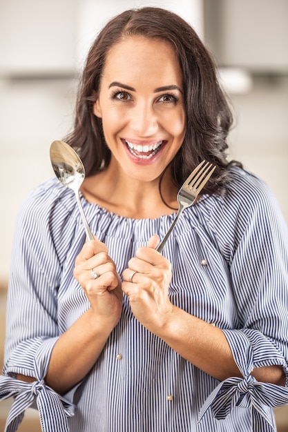 Happy woman holds fork and spoon indoors.