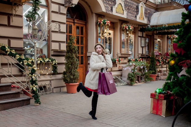 La donna felice tiene i sacchetti di carta con il simbolo della vendita nei negozi con le vendite a natale