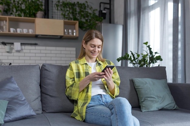happy woman at home reading from the phone and smiling sitting on the couch in the kitchen