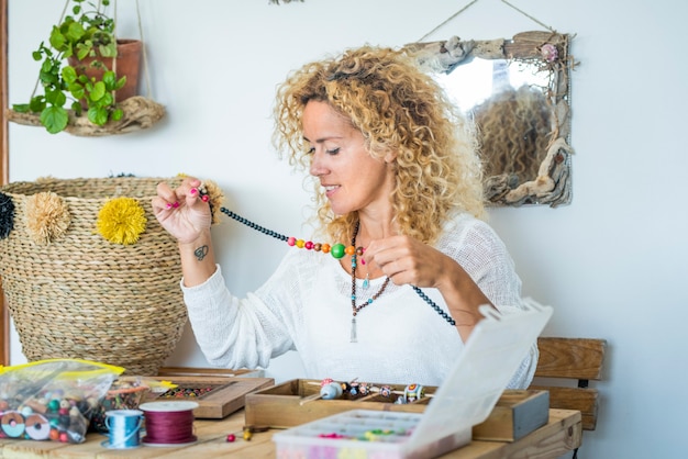 Happy woman at home work with beads and cords producing cheaper jewelry