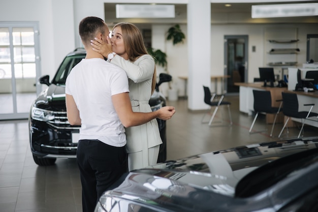 幸せな女性は、車のショールームで車を購入した後、夫を抱きしめます男性と女性は新しい車を購入します