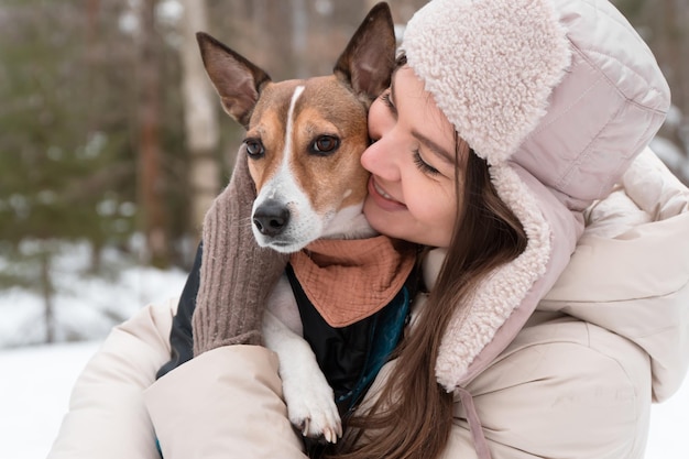 счастливая женщина обнимает собаку, гуляющую в зимнем парке