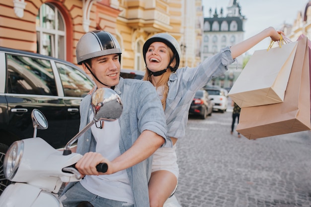 幸せな女は買い物袋を手に持って、彼のボーイフレンドがバイクを運転して白を楽しんでいます。