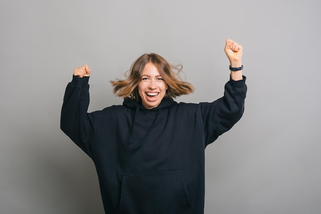 A happy woman is jumping with both her hands up while smiling at the camera