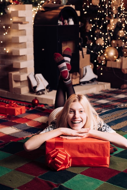 La donna felice è sdraiata sul pavimento con un regalo. periodo natalizio. ragazza bionda molto bella sopra l'albero di natale.