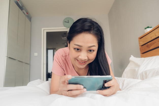 La donna felice sta giocando il gioco mobile sul suo letto.