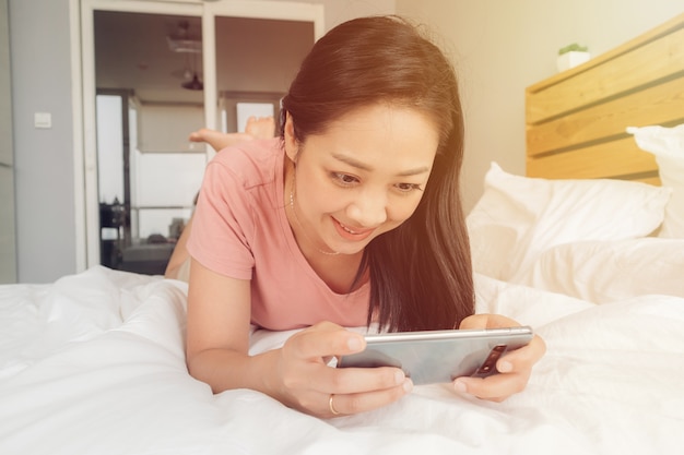 Happy woman is playing mobile game on her bed.