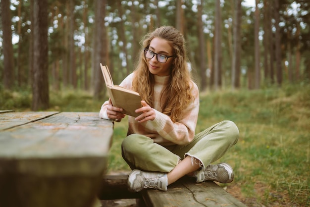 美しい森のテーブルに座って本を読んでいる幸せな女性リラックスしたライフスタイルのコンセプト