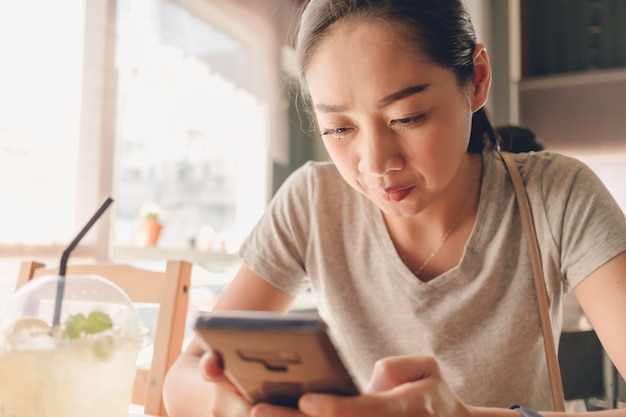 幸せな女は、コーヒーカフェでスマートフォンを使用しています。