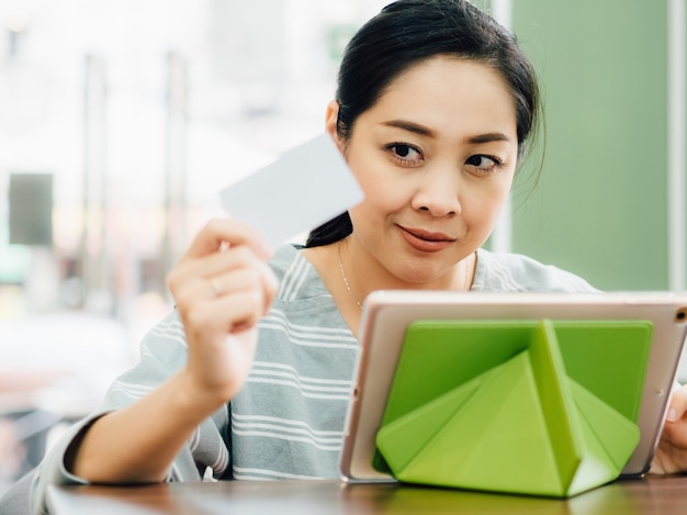 Happy woman is using a white mockup credit card for online shopping on tablet.