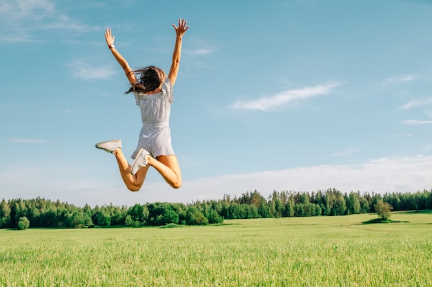 Happy woman jumping in green field against blue sky