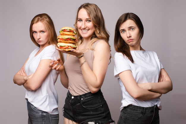 Happy woman keeping burger while sad girls standing near