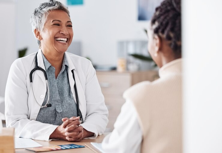 Photo happy woman laughing or doctor consulting a patient in hospital for healthcare help feedback or support mature medical or funny nurse with a person talking or speaking of test results or advice