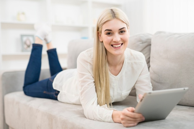 The happy woman lay on the sofa and hold a tablet