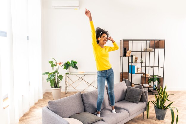 Happy woman listening music jumping and dancing on the sofa at home