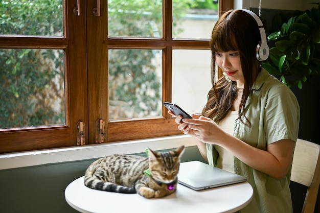 그녀의 귀여운 태비 고양이 테이블에 자고있는 동안 음악을 듣고 행복한 여자