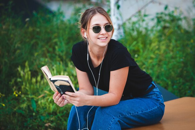 Happy woman listening to music with earphones and reading a book in the street