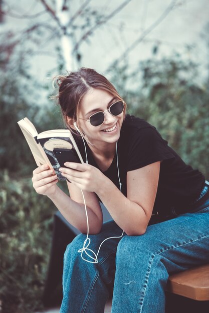 Foto donna felice che ascolta musica con gli auricolari e legge un libro per strada