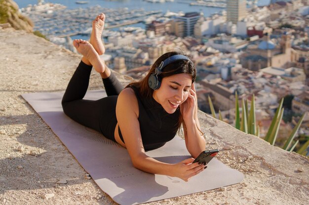 写真 幸せな女性は、街と海の背景に屋外で音楽を聴きます