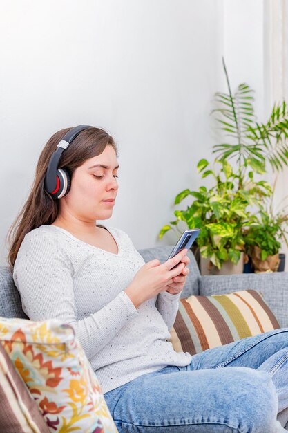 행복한 여성은 집에 있는 소파에 앉아 전화 콘텐츠를 듣고 시청합니다.