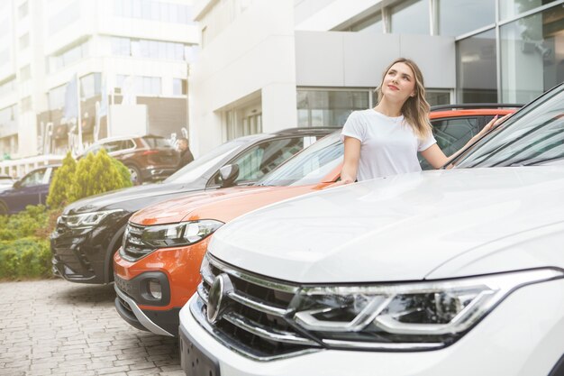 Happy woman looking away dreamily, choosing new car to buy on car dealership parking area, copy space