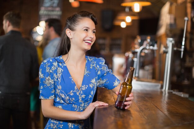 Счастливая женщина смотрит в сторону, держа бутылку пива