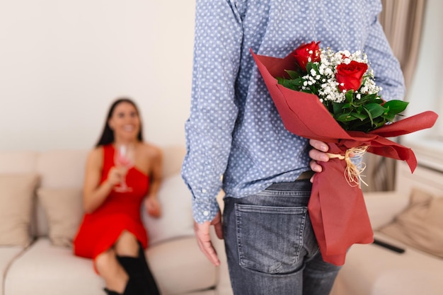 Happy woman looking at her boyfriend holding bouquet of roses behind his back Man holding flowers behind his back to surprise his girlfriend romantic happy couples on 8 March happy women's day