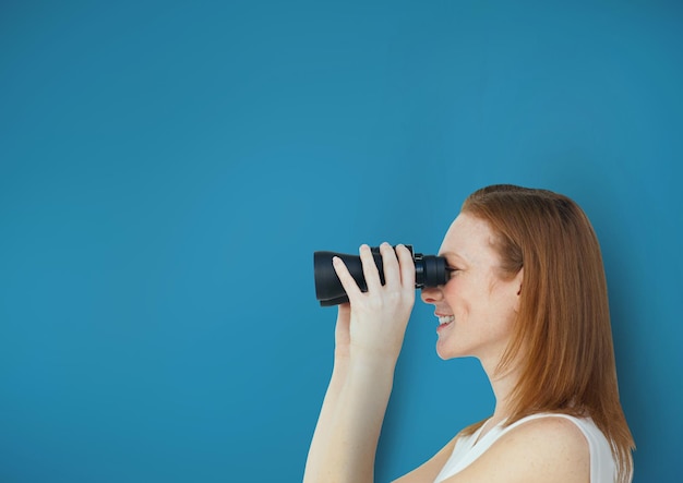 Happy woman looking through binoculars against blue background