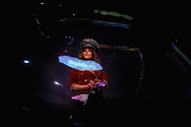 Фото Счастливая женщина фокусник цирк иллюзионист в стильной шляпе в шоу шоу мыльных пузырей на черном фоне