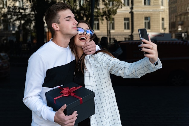 Photo happy woman makes selfie with her boyfriend. guy gives his girlfriend a gift and hugs her. smiling couple in love.