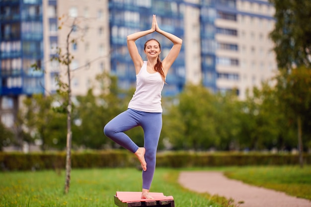 La donna felice fa l'addestramento di yoga sulla panchina del parco