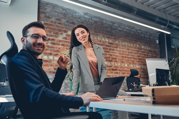 Foto felice donna e uomo in completo che conversano nell'ufficio del loft e guardano il davanti