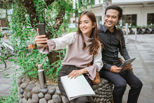 Happy woman and man using a smart phone taking selfie