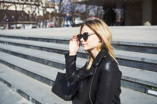 Happy woman model in a leather jacket walks down the street