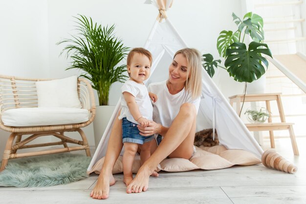 Happy woman mom and her little daughter playing in wigwam at home