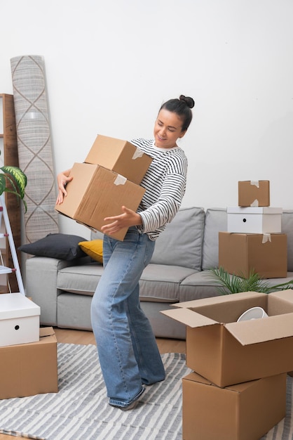 Happy woman moving into new home living room with pile of moving boxes welcoming belonging