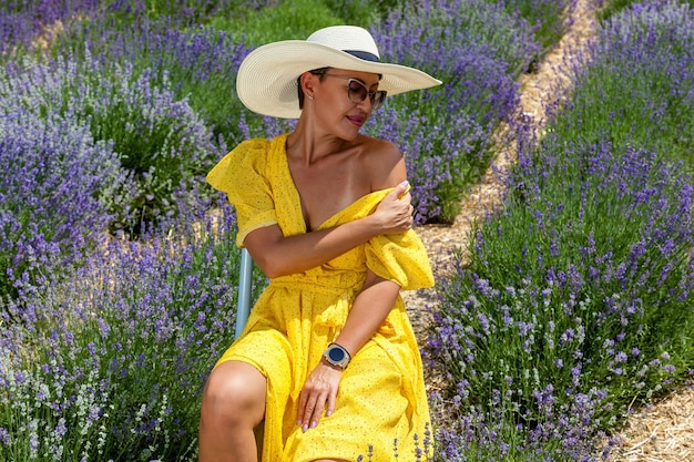 Happy woman near flowering bush lavender. Portrait of young smiling beautiful woman in yellow dress,