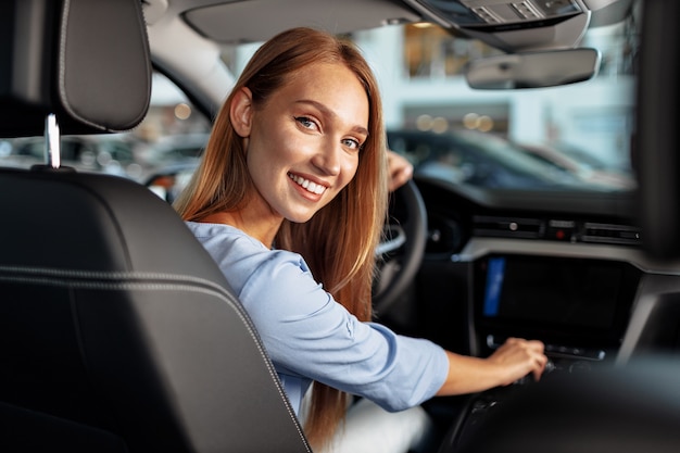 Happy woman new car owner sitting in driver seat and looking around